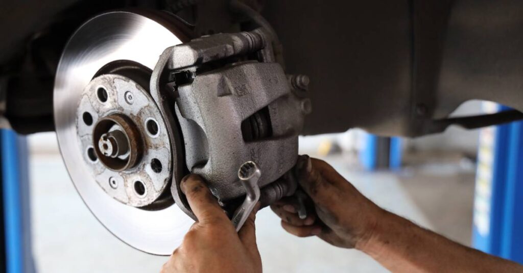 A pair of oil-stained hands of a mechanic or technician holding a vehicle's brake disc and a ratchet.