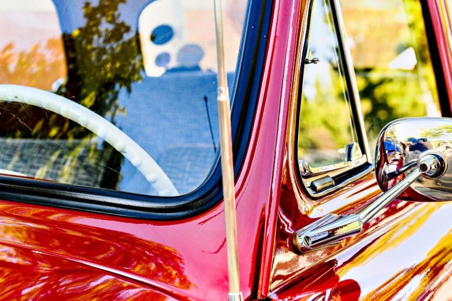 Here is a side view of one classic red car and a slew of classic black cars. Their headlights and front bumpers are in full view.