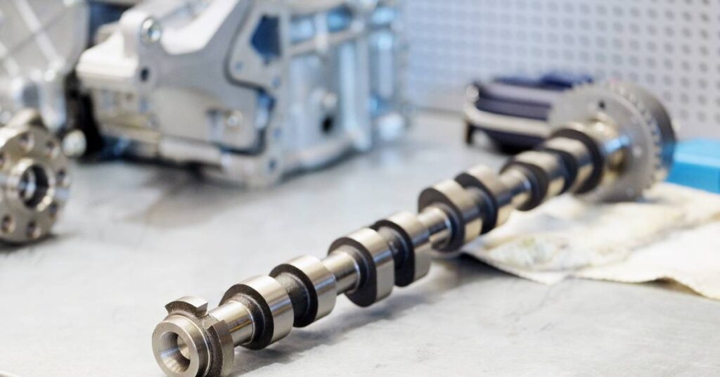A car engine camshaft sitting on a dirty cloth used for cleaning. Other car parts are on the left side of the table.