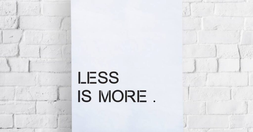 A white canvas stands against a white-bricked backdrop. At the bottom of the canvas, the words "less is more" appear in black.