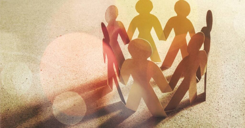 A group of cardboard people form a circle while touching hands. The light causes shadows to form.