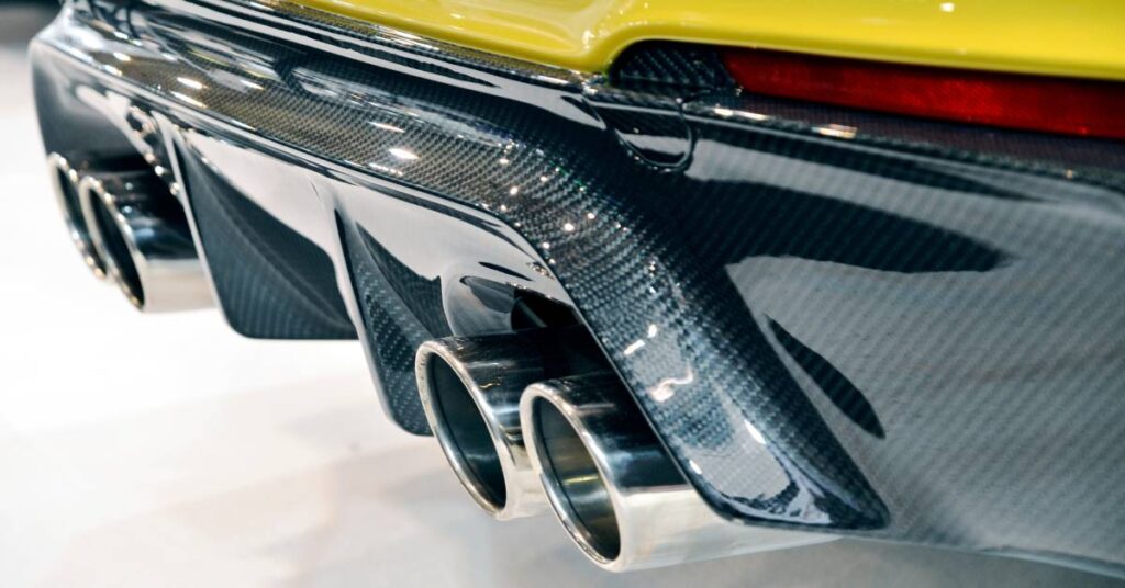 A close-up of a yellow sports car's exhaust pipe and bumper. The pipe and bumper are made of shiny, carbon fiber material.