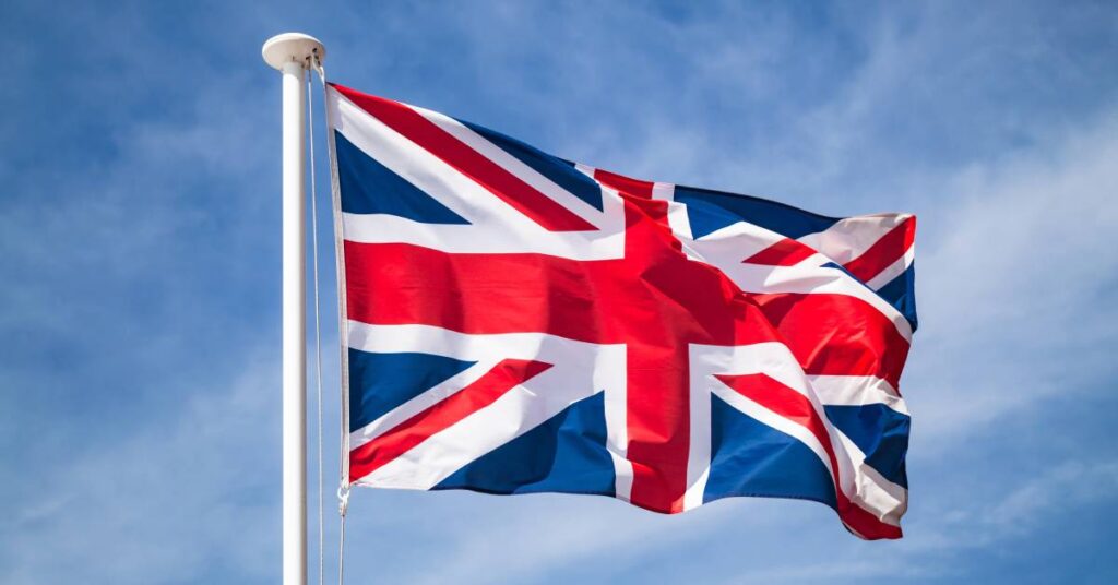 A white flagpole displaying the classic red, white, and blue United Kingdom flag, which billows in the wind.
