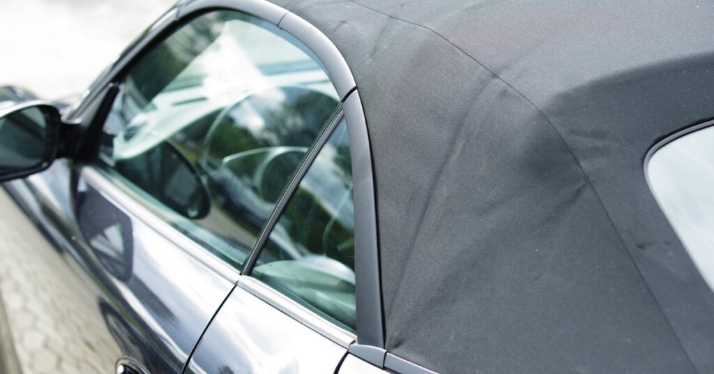 The back end of a chrome Volkswagen Cabrio with a black soft-top. The tiled ground it's parked on reflects in its side.