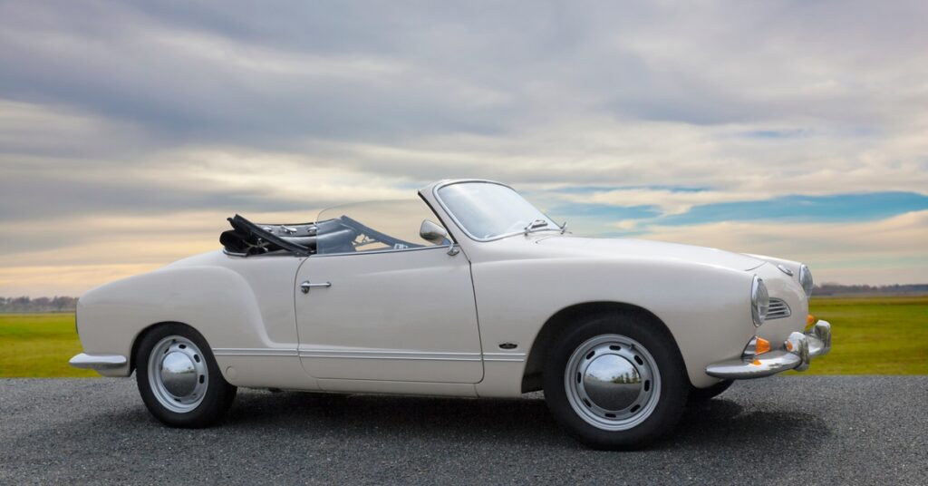 A white Volkswagen Cabrio parked on a blacktop with a field in the background. Its soft-top is pulled back.