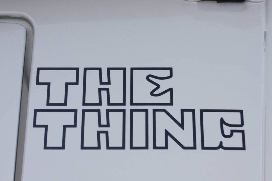 The gray metal surface of a vehicle with the phrase "THE THING" printed on its surface in hollow black letters.