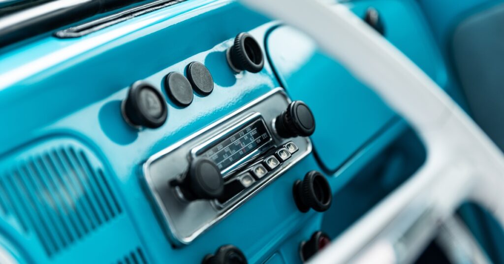 The dashboard of a retro vehicle with a bright blue surface and black knobs surrounding the built-in AM radio.