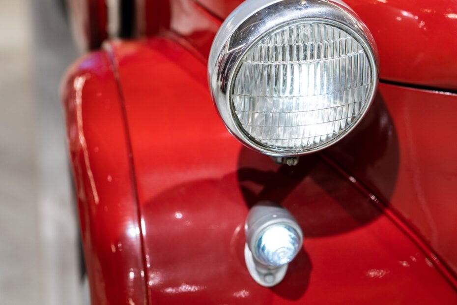 The front-right white headlight of a red Volkswagen Bettle. The vehicle shines with a clean glossy coating.