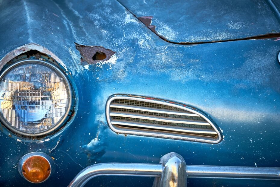 The front of a blue Volkswagen with chipping paint and a rusted chasis. Small dents appear in the metal trim.