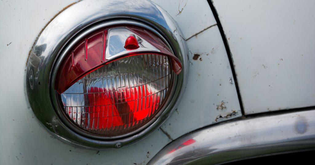 The red and white headlight of a white Volkswagen Bug with small spots of rust and cracks around the area.