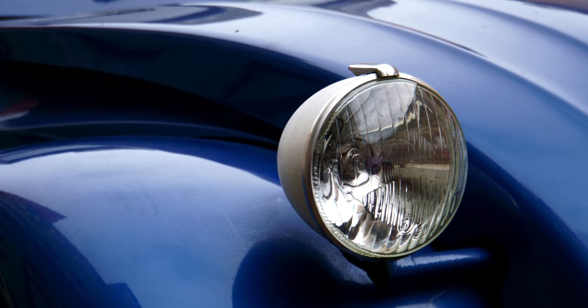 A close-up of the raised headlight of a royal-blue Volkswagen Beetle with a rippled hood and reflective finish.