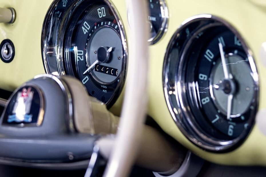 The dashboard of an old-school car colored a metallic light-yellow with various gauges to measure speed and RPM.