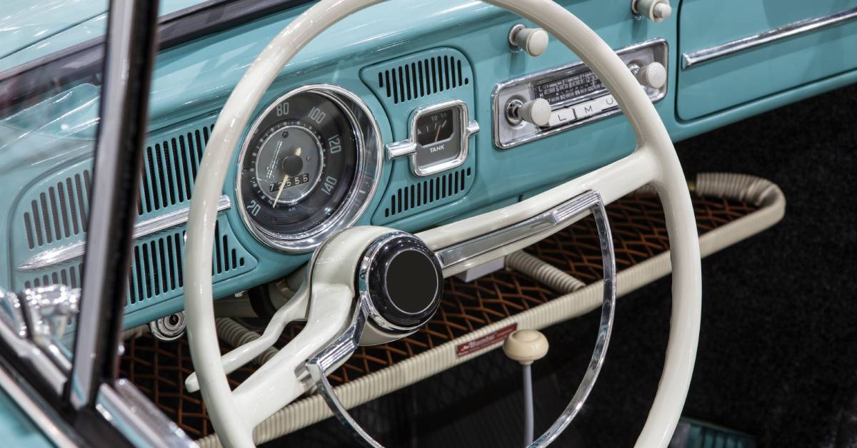 The empty interior of a vintage vehicle with blue coloring, white and silver accents, and black floor mats.