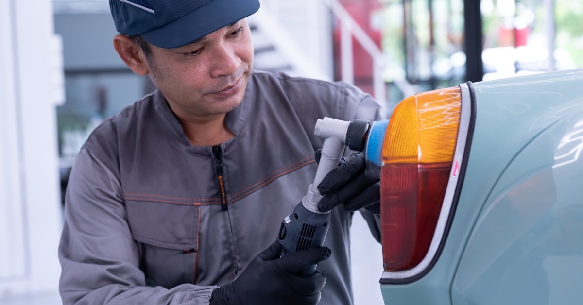 A young woman inspecting automobile components inside a warehouse and writing notes in a blue folder.