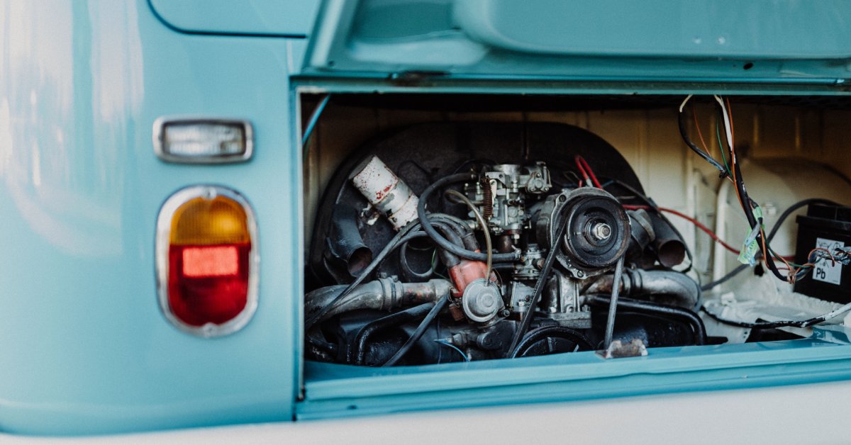 A vintage light blue Volkswagen Type 2 Microbus with the rear hatch open, showing the air-cooled engine and exposed wiring.