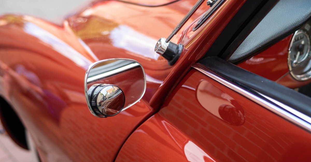 A classic red car with reflective paint and a glossy chrome window trim visible along the door frame.