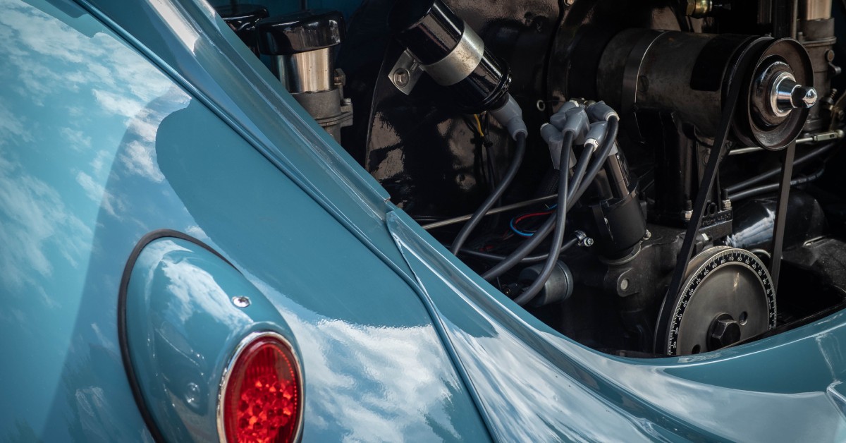 An open hood on a light blue vintage car showing the engine, belts, and other mechanical components.