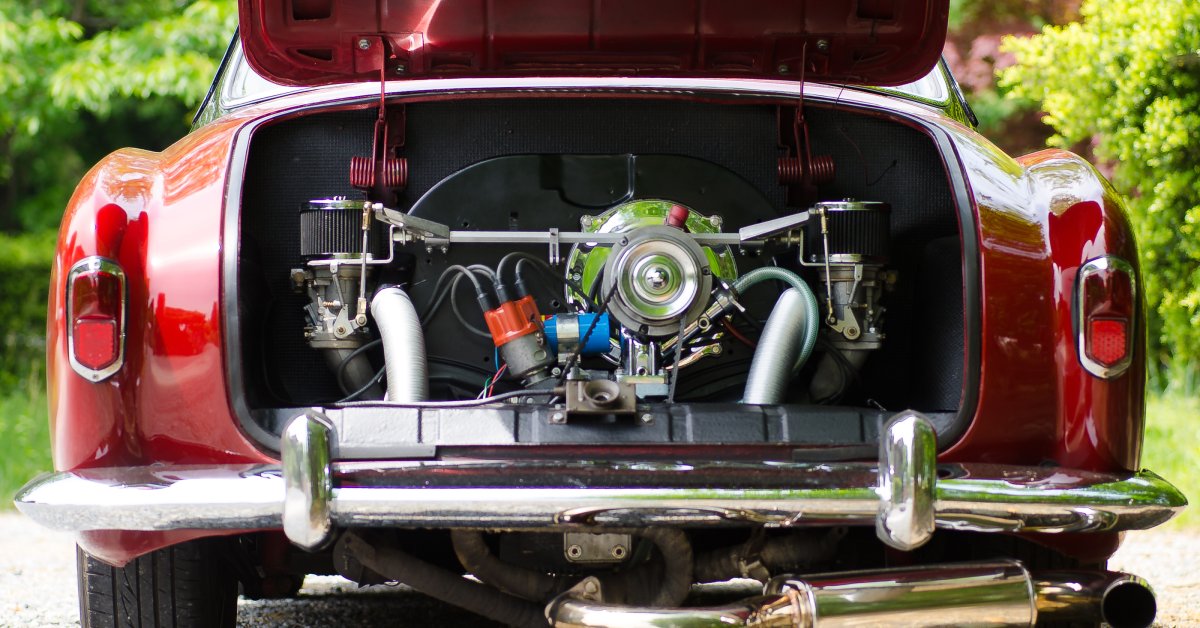 A parked vintage red Karmann Ghia with its rear engine compartment open, revealing an air-cooled motor.