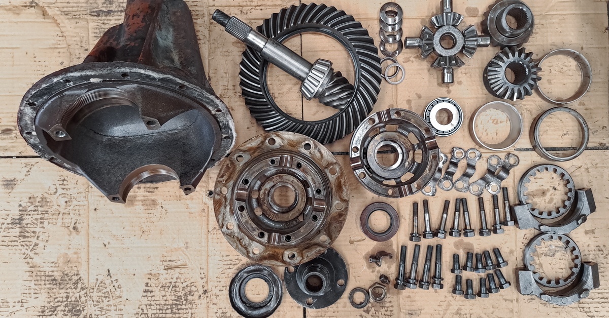 All different types of old car transmission parts laid out on a table. Some are older and covered in rust.