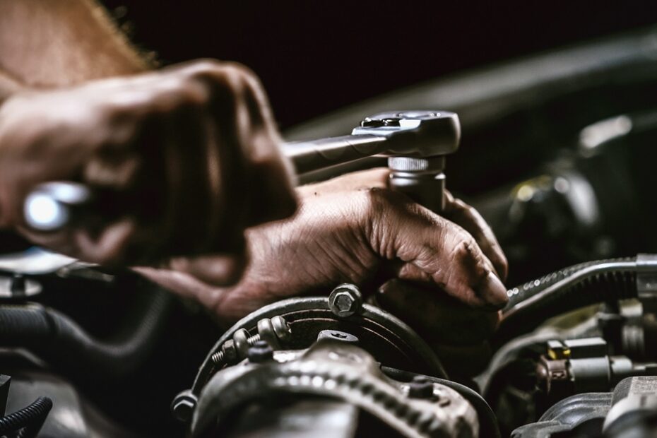 A close-up of a person's hands holding mechanic tools and fixing up parts under a vehicle's hood.