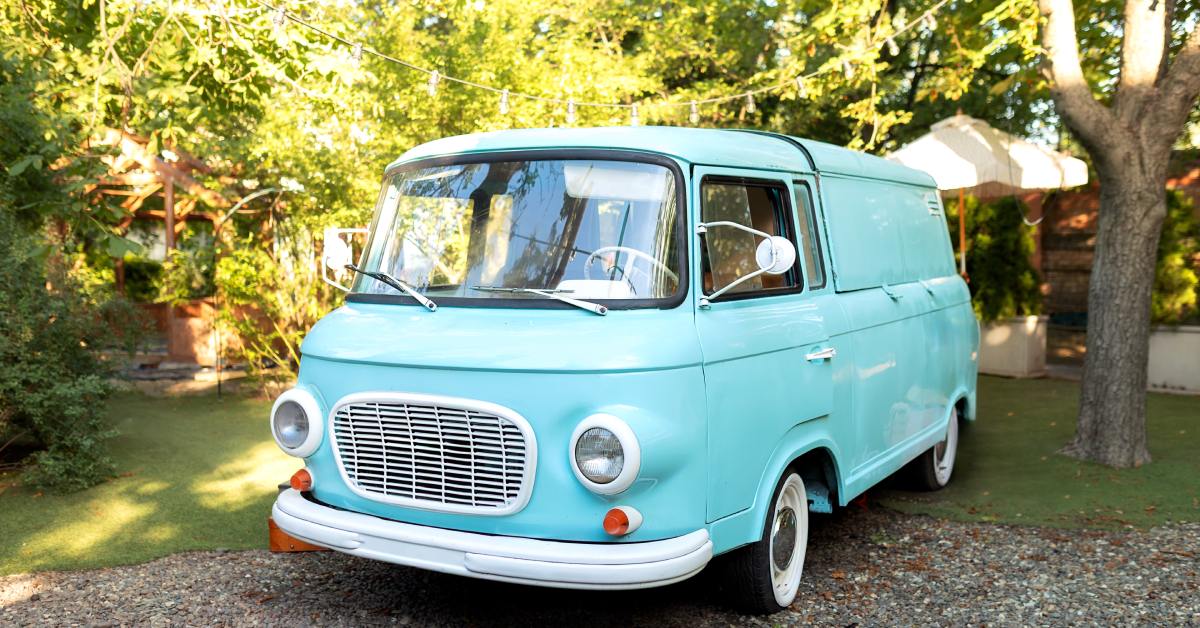 A light blue classic bus with white accents on the lights, mirrors, hub caps, and bumper, parked outdoors.