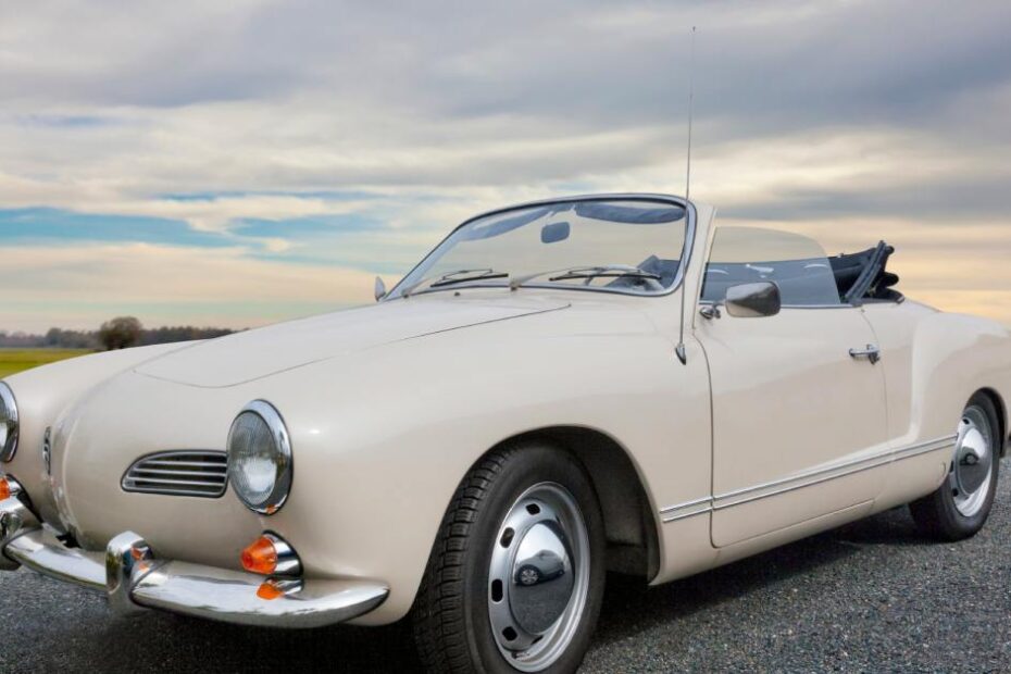 A Karmann Ghia sits on a blacktop road on a cloudy day. The clouds are gloomy and the grass is green.