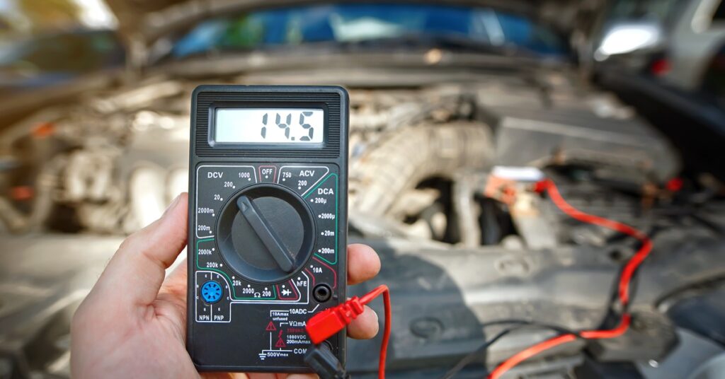 A close-up of a car battery voltage testing instrument with a reading of 14.5 on the small screen.