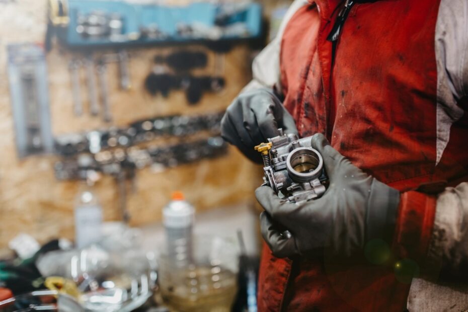 A close-up of a mechanic working on a carburetor part for a vehicle, oil smeared on his gloves and shirt.