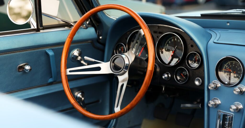 A close-up of a steering wheel and blue front console of a classic car from the interior of the vehicle.