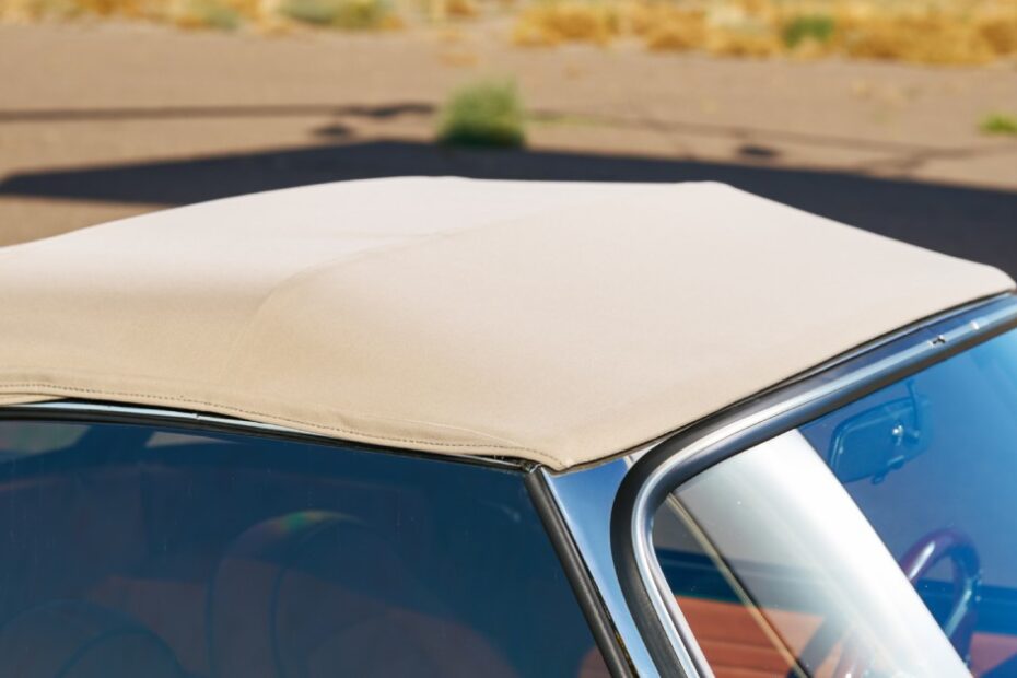 A close-up of a tan fabric top on a convertible classic car with a desert landscape in the background.